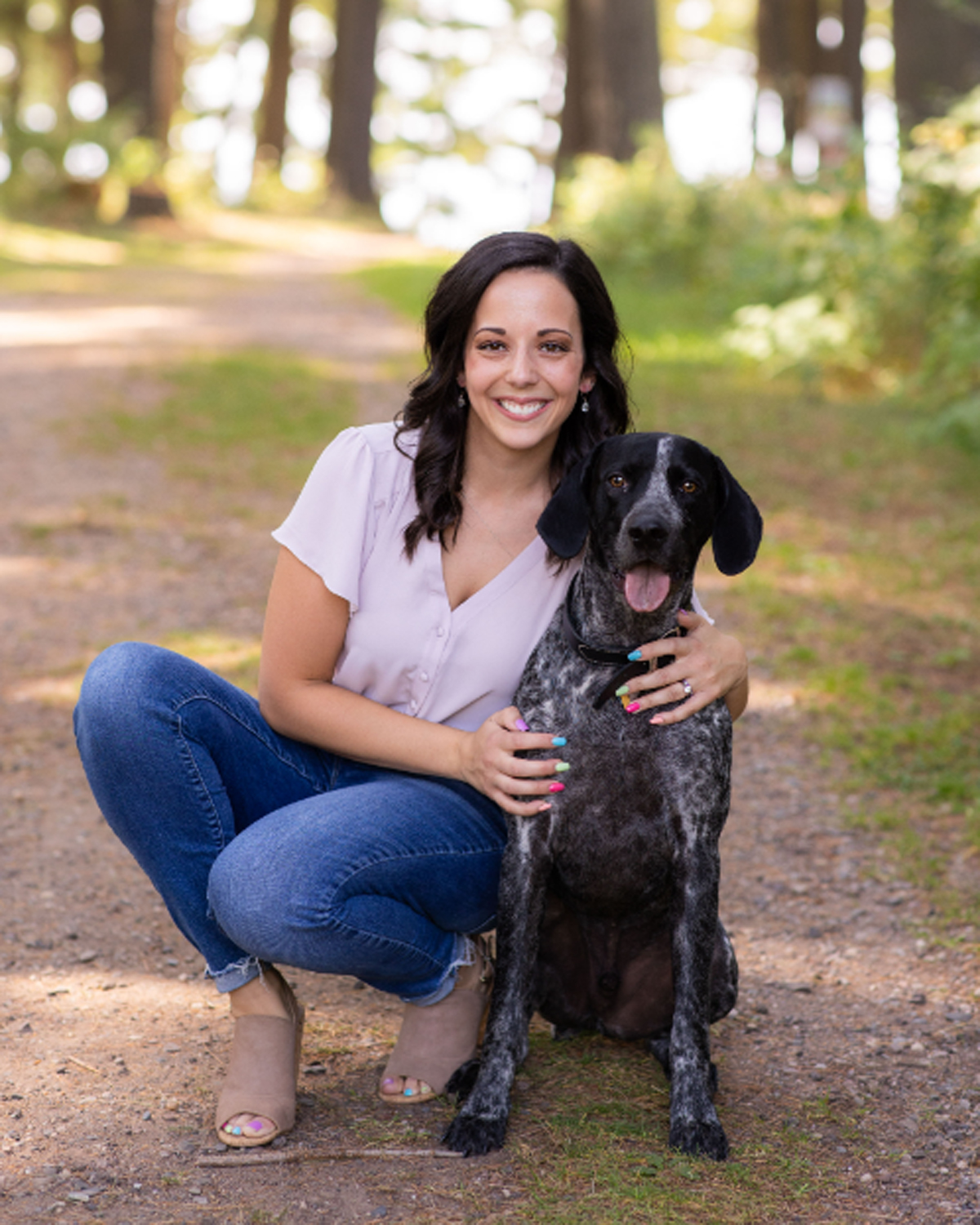 A person sitting on a dirt path with a dogDescription automatically generated